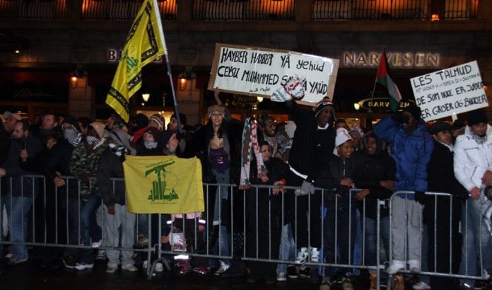 Utenfor Stortinget 8. januar 2009: Flagg for terrororganisasjonen Hizbollah og plakat som minner jødene (yehud) om Hayber (sted hvor jøder ble drept og fordrevet på 600-tallet). «Muhammeds hær vil komme tilbake» truer siste setning. Stein og andre tunge gjenstander regnet ned over venner av Israel, som avholdt en fredelig markering utenfor Stortinget. (Foto: Odd Østtveit) Utenfor Stortinget 8. januar 2009: Flagg for terrororganisasjonen Hizbollah og plakat som minner jødene (yehud) om Hayber (sted hvor jøder ble drept og fordrevet på 600-tallet). «Muhammeds hær vil komme tilbake» truer siste setning. Stein og andre tunge gjenstander regnet ned over venner av Israel, som avholdt en fredelig markering utenfor Stortinget. (Foto: Odd Østtveit)