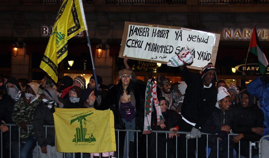 Da Israel-venner holdt en støttemarkering for Israel i Oslo 8. januar 2009 holdt noen av motdemonstrantene opp dette banneret. Teksten er en trussel om å gjenta Muhammeds massakre av de tre jødiske stammene i Hayber. Legg også merke til de gule flaggene for terrororganisasjonen Hizbollah. (Arkivfoto: Odd Østtveit)