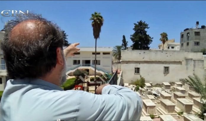 Erkebiskop Alexios peker mot stedet der raketter har blitt avfyrt fra kirkens område. (Foto: Skjermdump fra CBN) Erkebiskop Alexios peker mot stedet der raketter har blitt avfyrt fra kirkens område. (Foto: Skjermdump fra CBN)